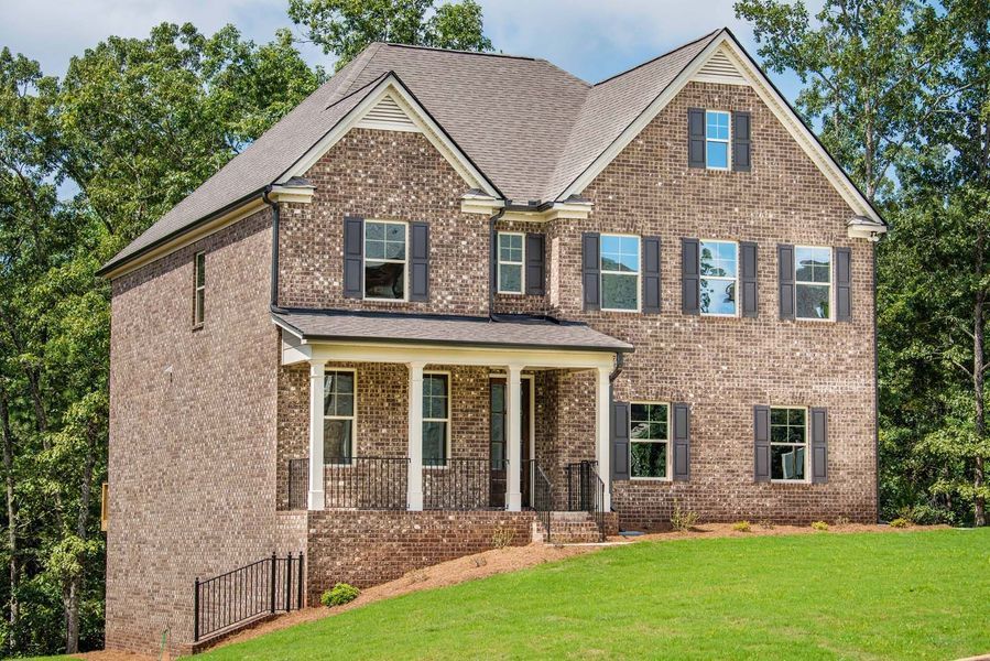 Brick two-story house with a porch, gray shutters, and a sloping green yard, surrounded by trees.