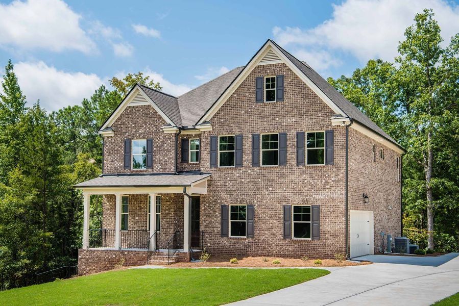 Two-story brick house with gray shutters, a porch, and a driveway on a grassy hill.