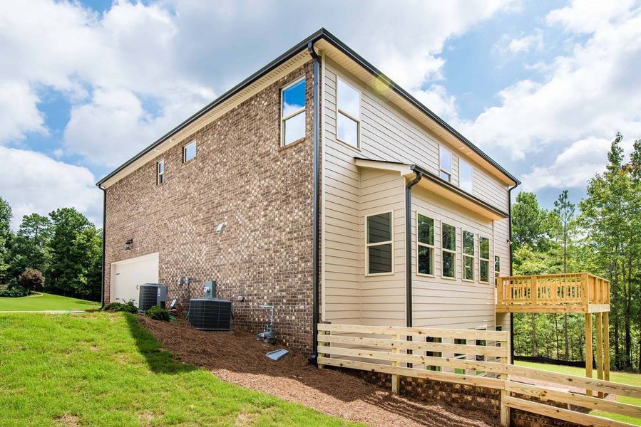 Two-story house with brick and tan siding, a wooden deck, and green lawn under a blue sky.
