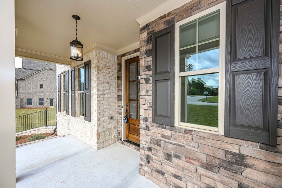 Porch of a house with stone siding and a wooden door. Dark shutters flank a window.