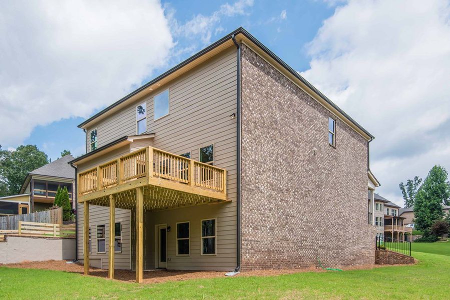 Two-story house with a wooden deck and brick siding, set against a cloudy sky.