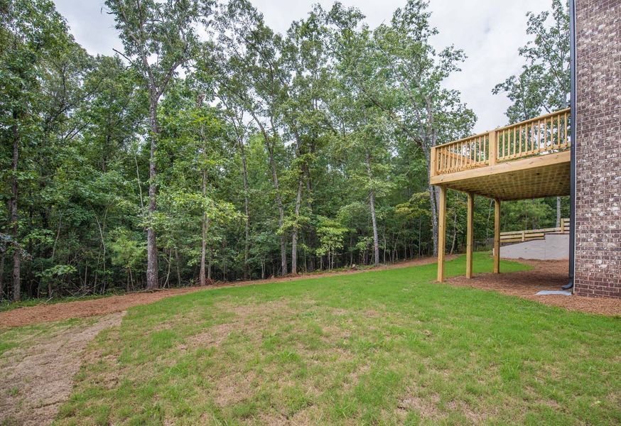 Lawn with a wooden deck, surrounded by trees and brick wall, under a cloudy sky.
