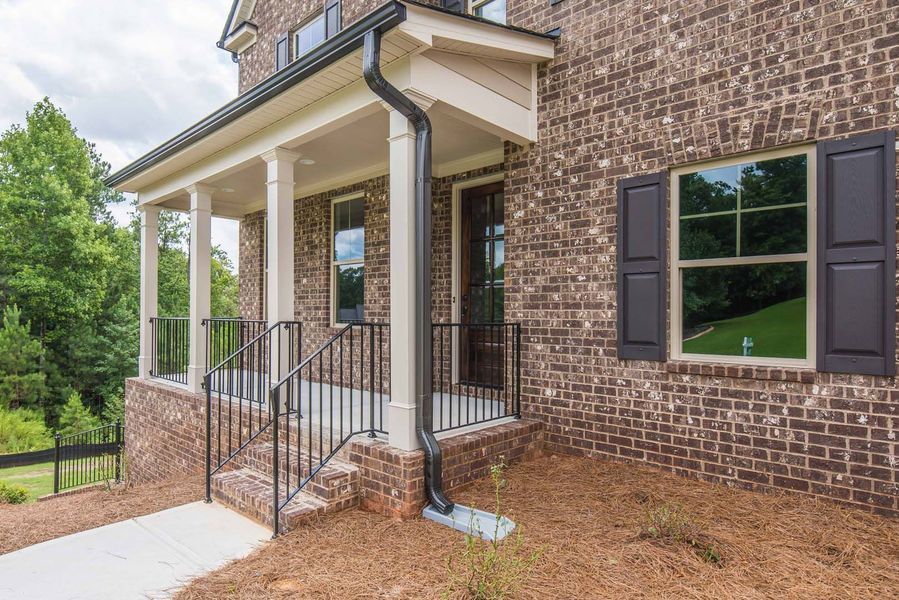 Brick home exterior with a front porch, black shutters, and dark gutter.