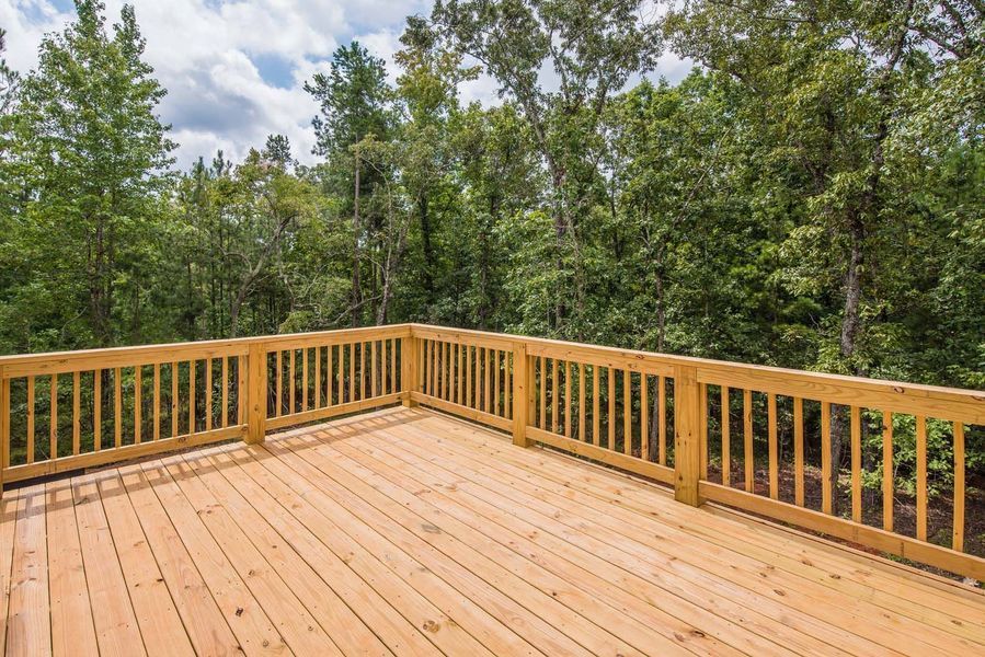 Wooden deck with railing overlooking a lush green forest under a partly cloudy sky.