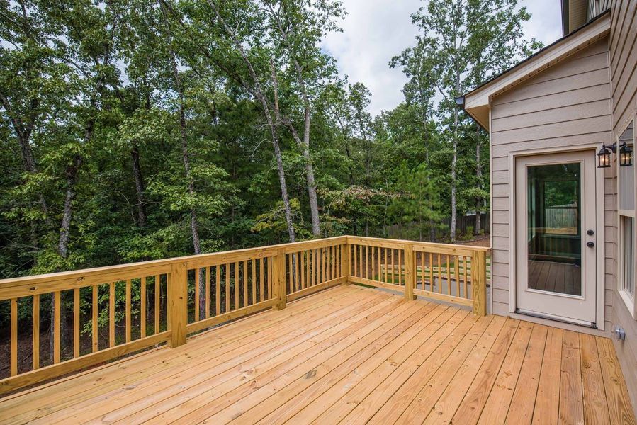Wooden deck attached to a beige house, surrounded by trees.