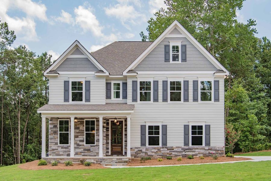 Two-story house with gray and white exterior, blue shutters, and stone accents, on a green lawn.