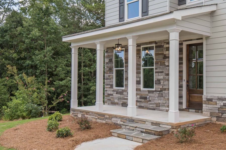 Exterior of a home with a stone facade and covered porch, steps, and landscaping.