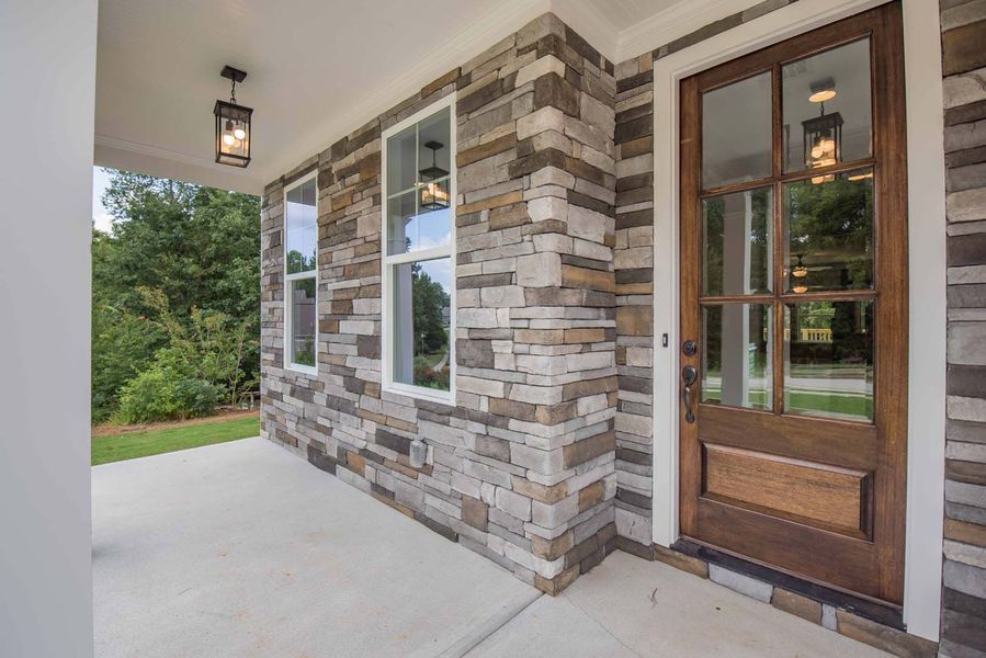 Stone facade porch with brown door, windows, and hanging light.