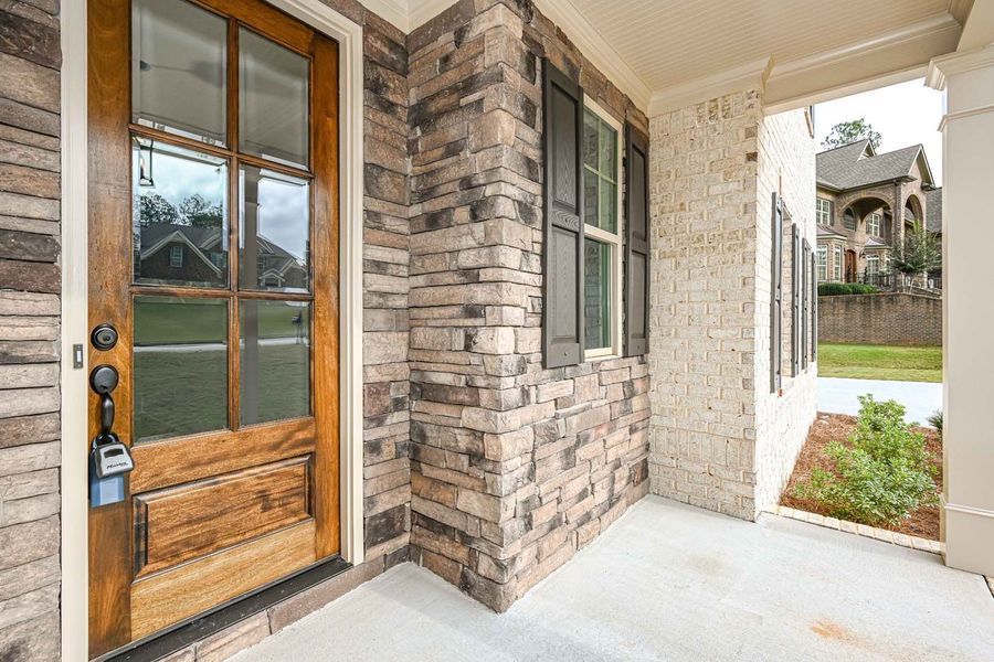 Wooden front door with key lockbox next to stone and brick facade. Porch.