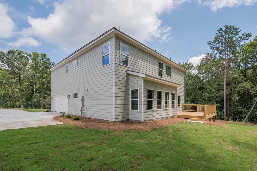 Two-story beige house with a wooden deck on a grassy lawn under a partly cloudy sky.