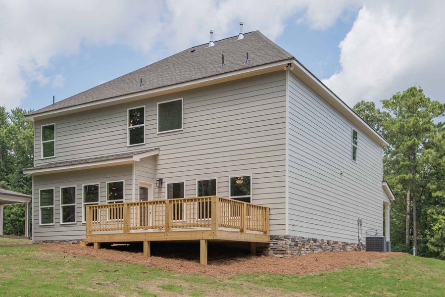 Back of a two-story house with a wooden deck and gray siding, under a cloudy sky.