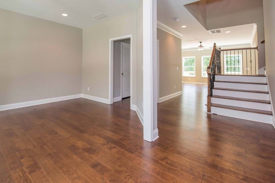 Empty interior space with hardwood floors, neutral walls, staircase, and doorway.