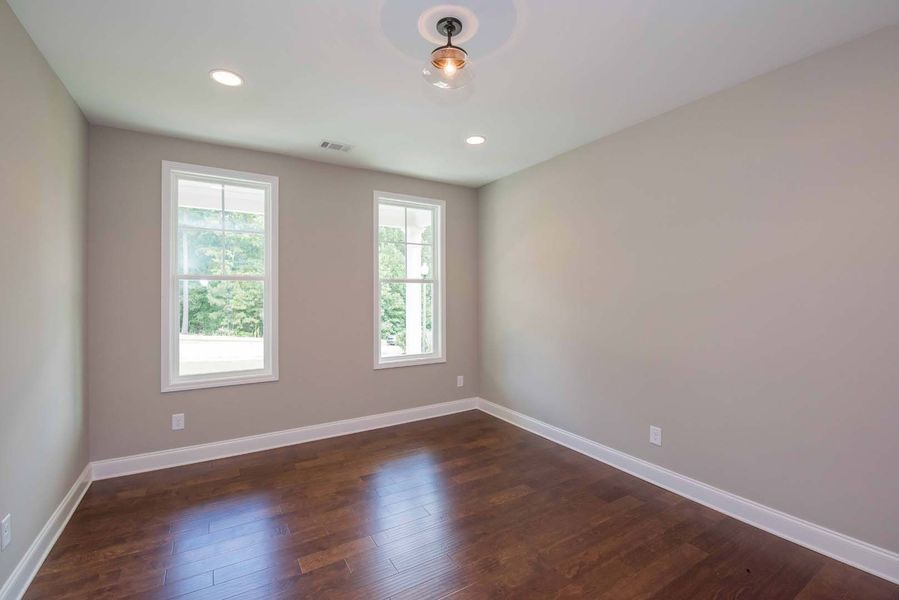 Empty room with brown hardwood floors, light gray walls, two windows, and a ceiling light.