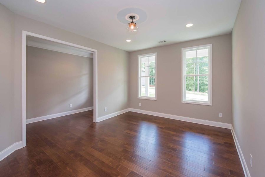 Empty room with hardwood floors, two windows, and a doorway to another room; neutral colors.