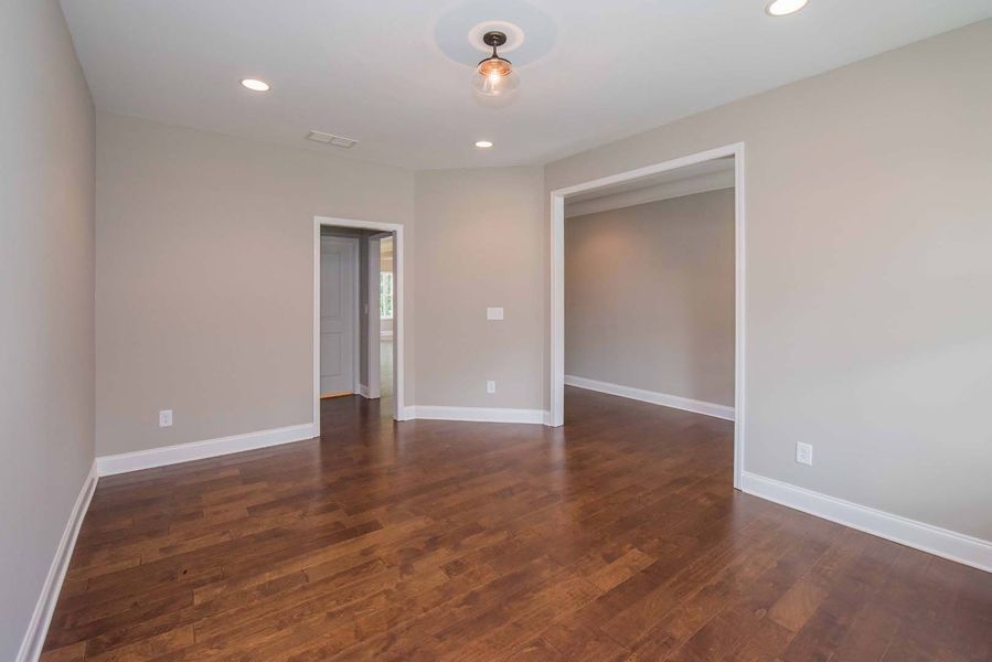 Empty room with wood floor, light gray walls, and doorways.