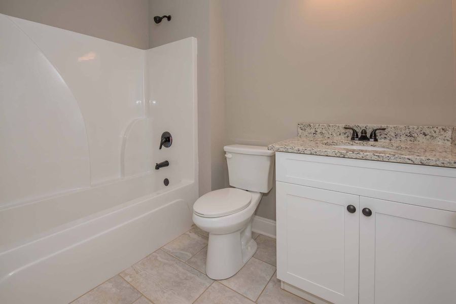 White bathroom with a bathtub, toilet, and sink. Light-colored walls and countertop.