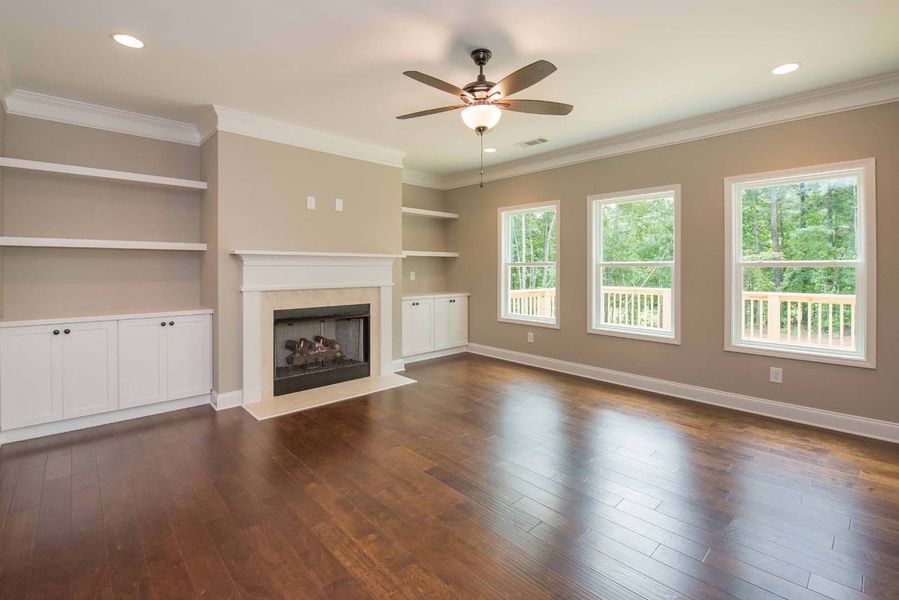 Living room with fireplace, built-in bookshelves, three windows, dark wood floor, and a ceiling fan.