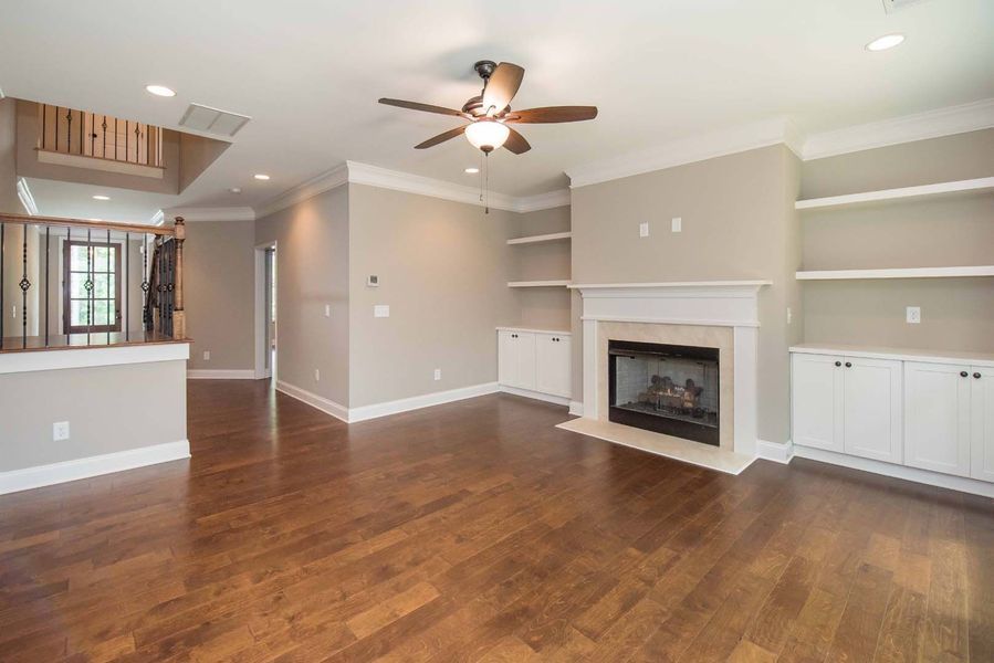 Living room with fireplace, built-ins, hardwood floors, and ceiling fan.