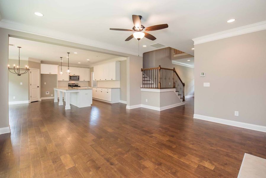 Open-concept living room with wood floors, leading to a white kitchen, and a staircase.