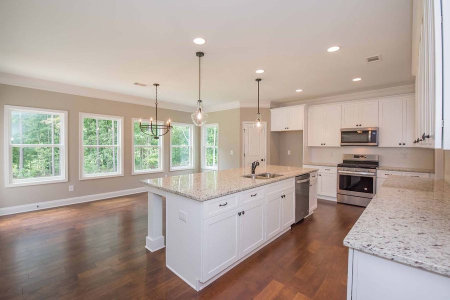Bright kitchen with white cabinets, granite countertops, island, and windows.