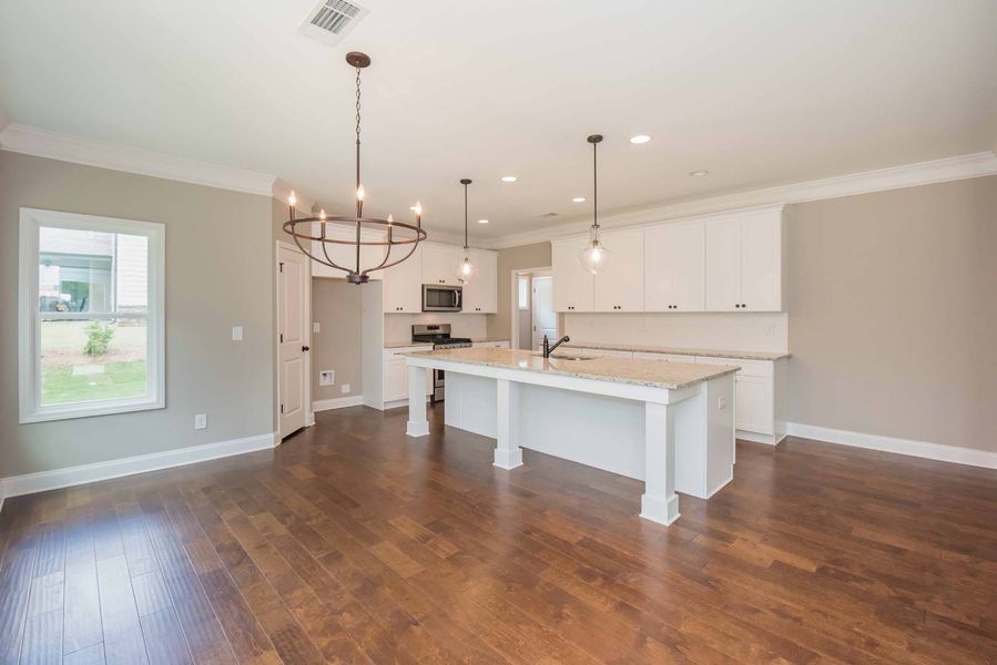 Spacious kitchen with white cabinets, large island, wooden floor, and chandelier.