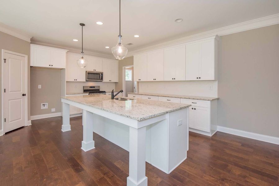 White kitchen with island, granite countertops, and dark wood floors.