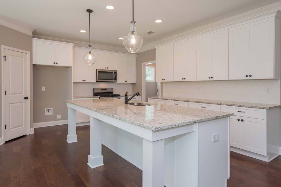 White kitchen with granite countertops, white cabinets, dark wood floors, and two pendant lights.