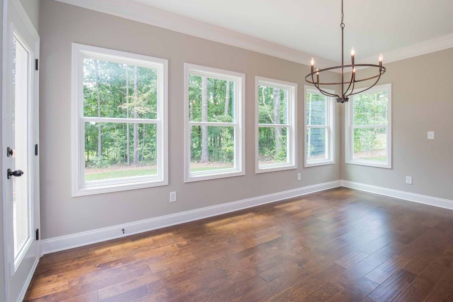 Empty room with hardwood floor, light walls, multiple windows, and a chandelier.