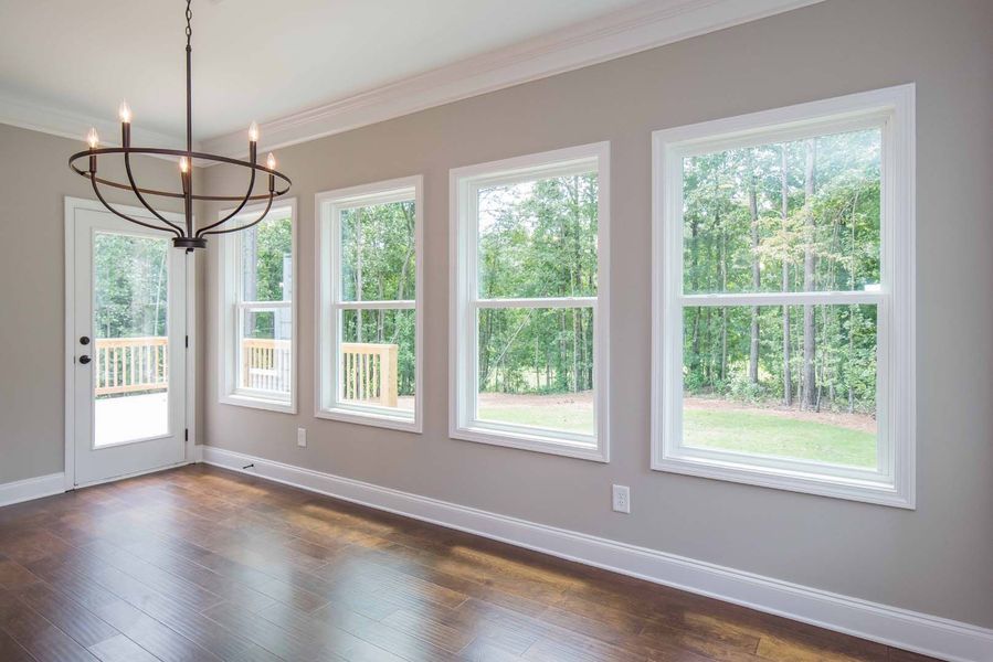 A room with windows, a door, and a chandelier, overlooking a green yard, with wooden floors and tan walls.