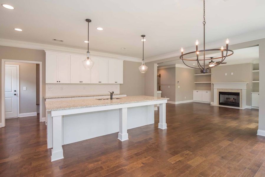 Modern kitchen with white cabinets, island, and hardwood floors; neutral walls, fireplace in the background.
