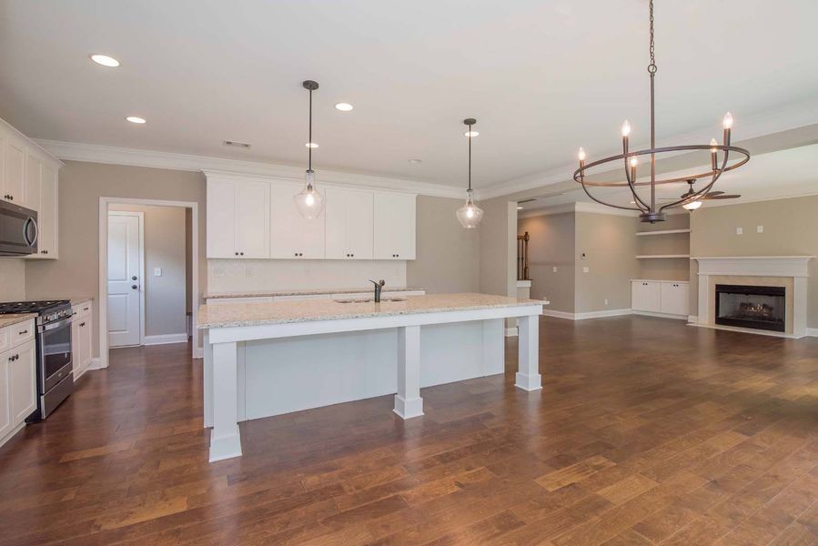 Open-concept kitchen with white cabinets, island, and dark wood floors. Light fixtures illuminate the space.
