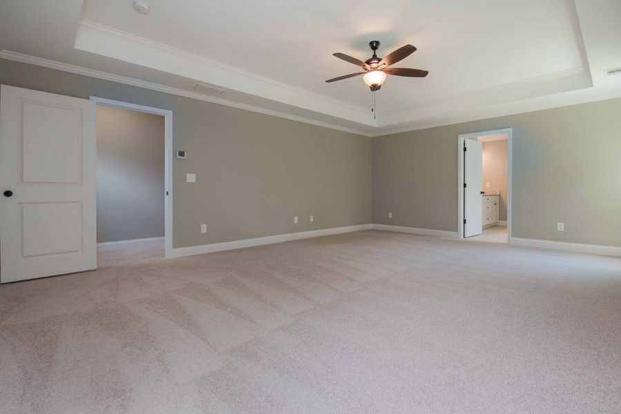 Empty bedroom with neutral walls and carpet, open doorways, and ceiling fan.