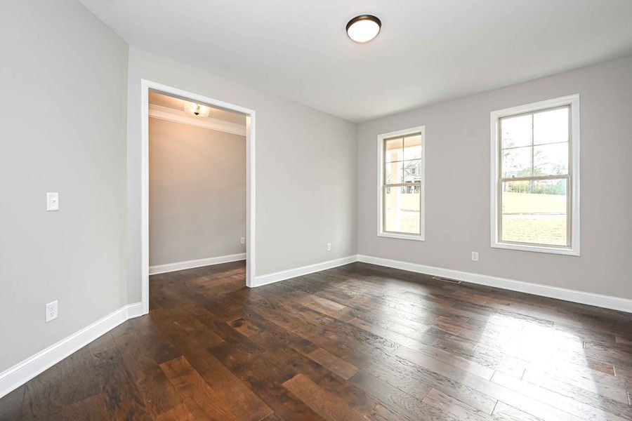 Empty room with dark hardwood floors, gray walls, white trim, and two windows.