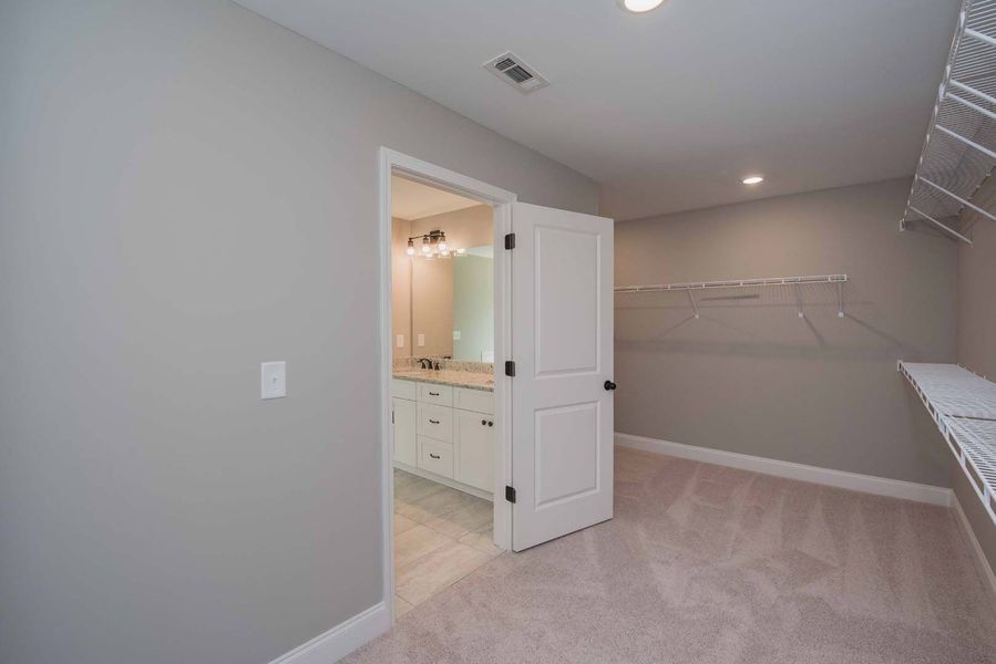 Empty walk-in closet with white wire shelving, light gray walls, and door to a bathroom.