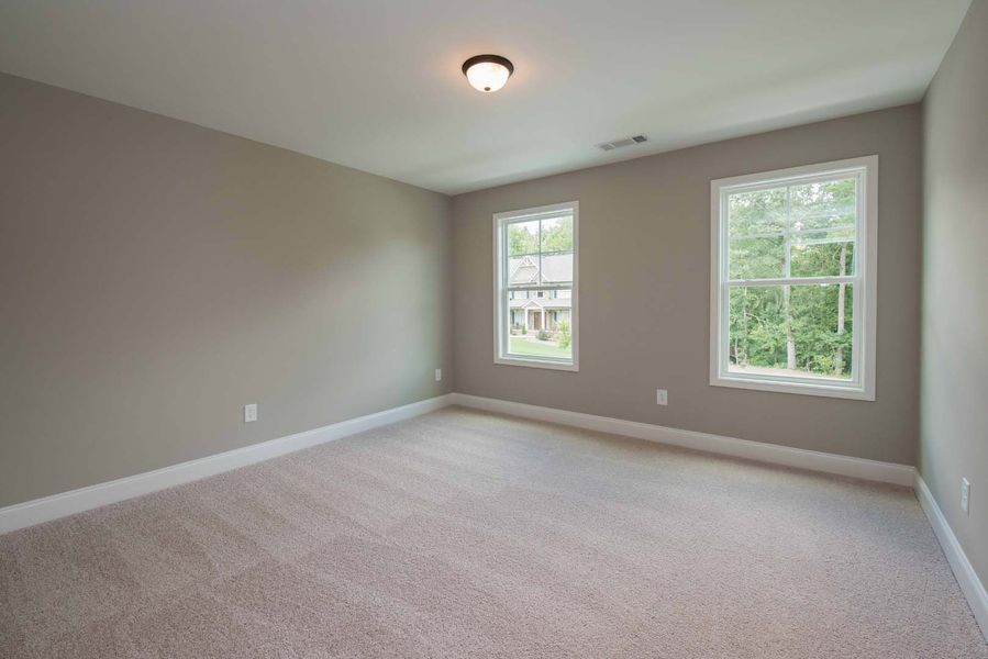 Empty bedroom with beige walls, carpet, and two windows.