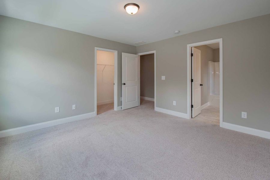 Empty bedroom with gray walls, white trim, and beige carpet; three doorways.