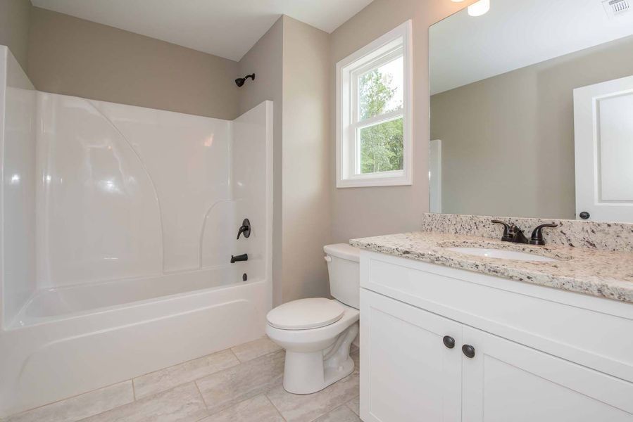 Bathroom with white bathtub, vanity, toilet, window, and light gray walls.