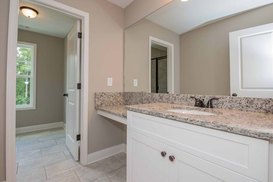 Bathroom with white vanity, granite countertop, and a door leading to another room.