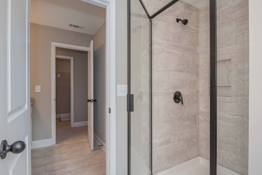 Hallway leading to a walk-in shower with gray tile and black fixtures.