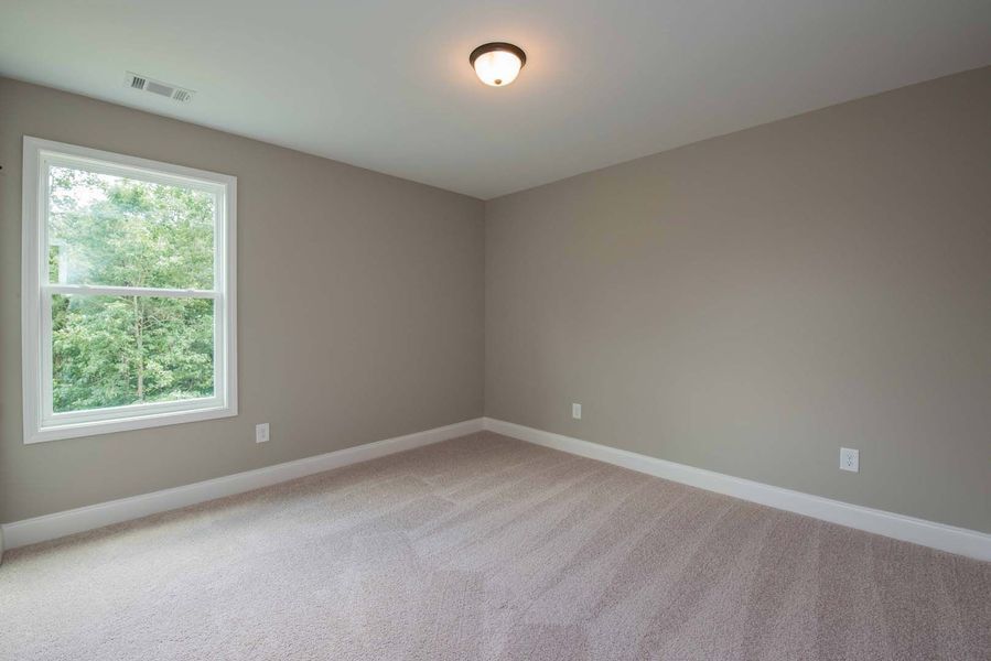 Empty beige-walled room with window, carpet, and ceiling light; neutral interior.