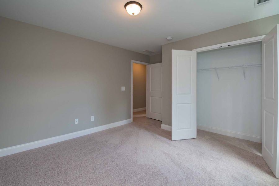 Empty bedroom with beige walls, carpet, and a white closet.