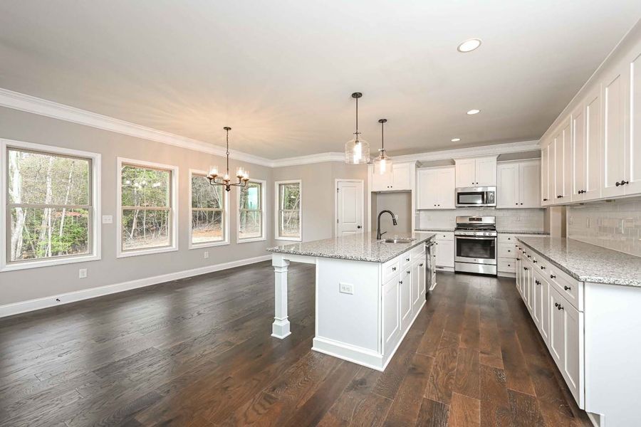 Spacious white kitchen with island, hardwood floors, and gray walls. Natural light from large windows.
