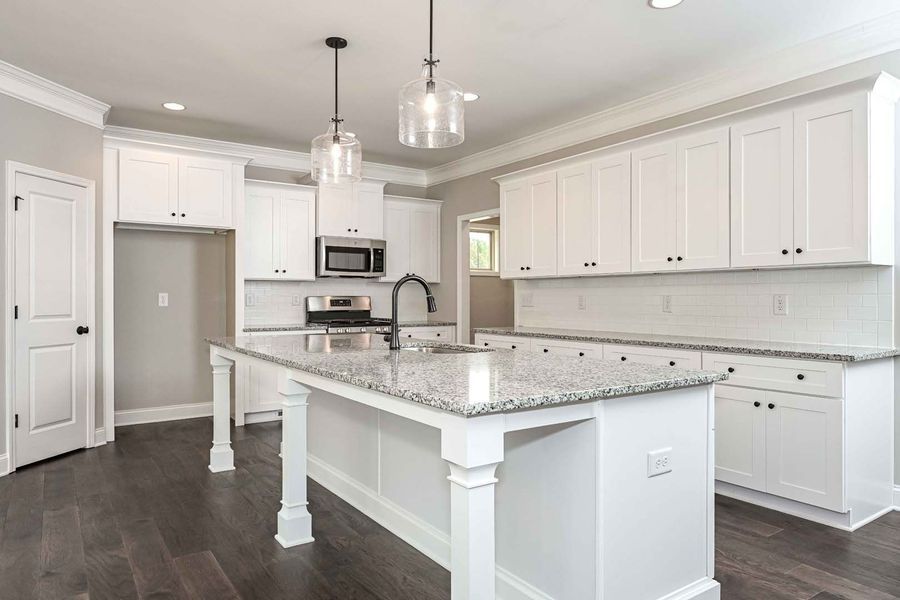 White kitchen with island, granite countertops, stainless steel appliances, and dark wood floors.