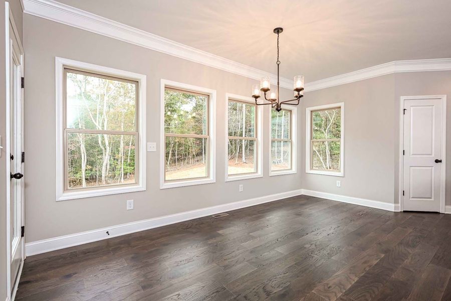 Empty dining room with dark wood floors, white trim, and windows overlooking trees.