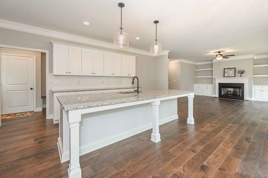 Open-concept kitchen with white cabinets, gray countertops, and dark wood flooring. Includes an island, and a fireplace.