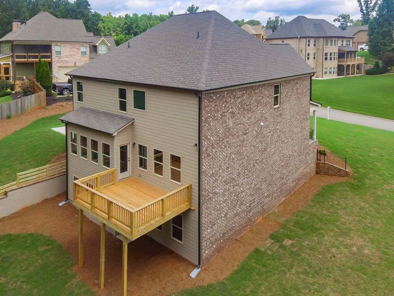 Back of a two-story house with a wooden deck, brick and tan siding, set on a grassy lawn.