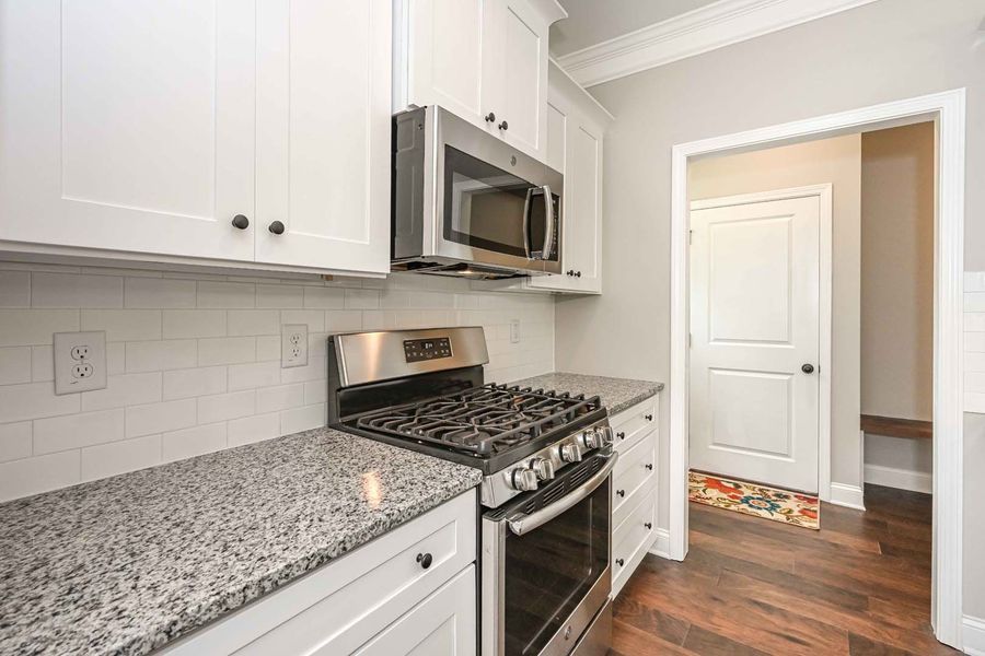 White kitchen with granite countertops, stainless steel appliances, and a doorway.