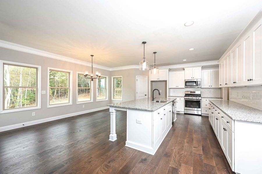 Modern kitchen with white cabinets, island, granite countertops, stainless steel appliances, and hardwood floors.