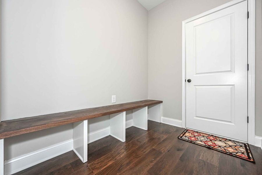 A wooden bench with white supports in a room with a door and dark wood flooring.