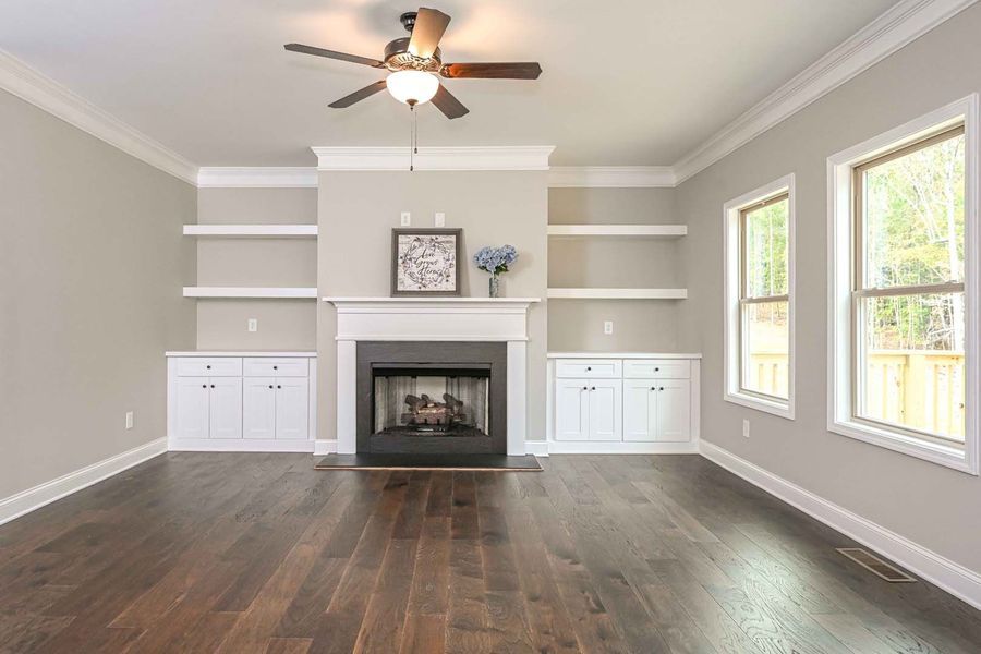 Living room with fireplace, built-in shelves and cabinets, dark wood floors, and large windows.
